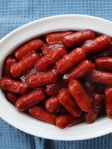 Little smokies with bbq sauce and chilli sauce in a serving dish.