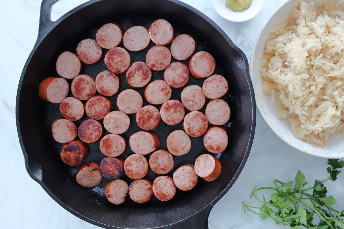 Sliced kielbasa browning in a skillet with oil, creating flavor for a classic kielbasa and sauerkraut recipe.