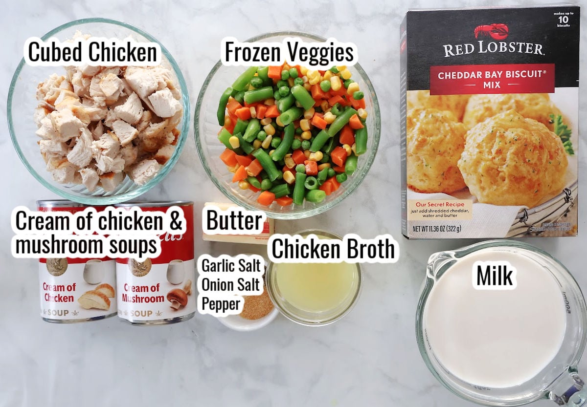 Chicken cobbler ingredients including cubed chicken, frozen veggies, butter, chicken broth,  cream of soup and Red Lobster cheddar bay biscuit mix mixed with milk.