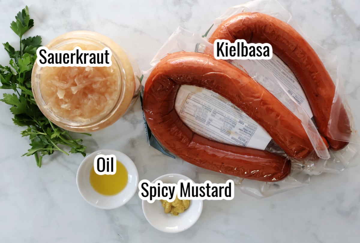 Ingredients for kielbasa and sauerkraut including sliced kielbasa, drained sauerkraut, mustard, oil, and fresh parsley.