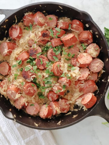 Kielbasa added back into the skillet with sauerkraut to finish cooking the dish.