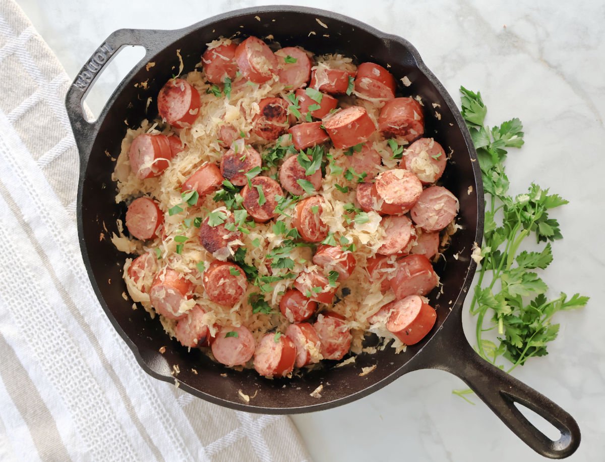 Kielbasa added back into the skillet with sauerkraut to finish cooking the dish.