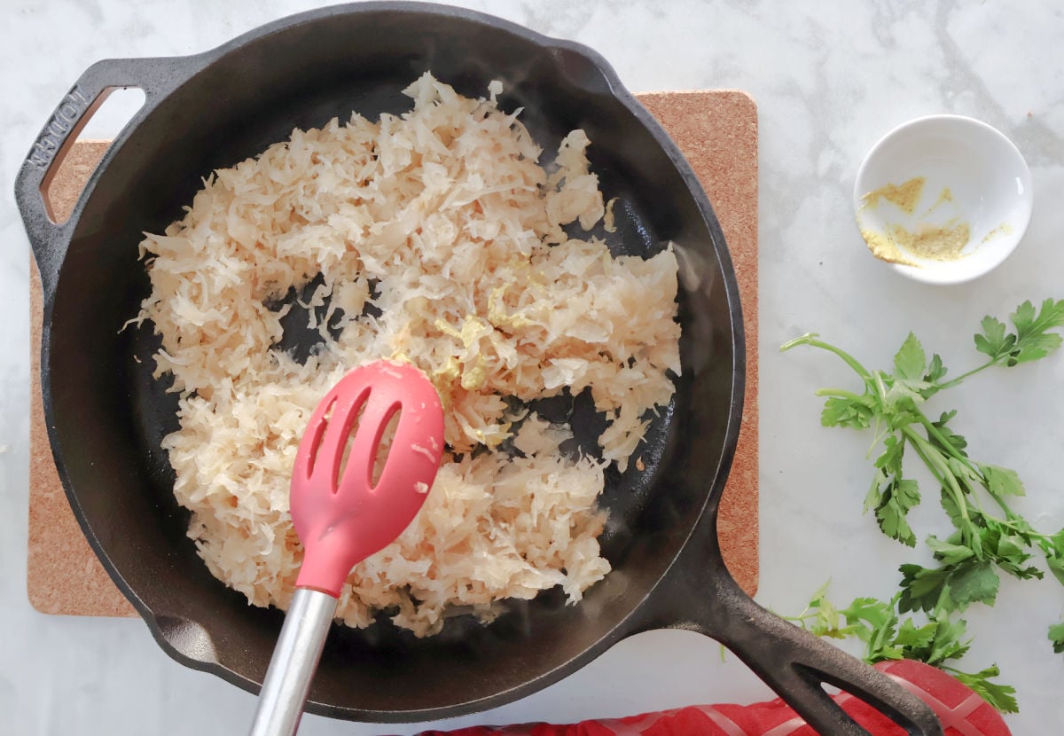 Drained sauerkraut added to a skillet with mustard and browned bits for kielbasa and sauerkraut.