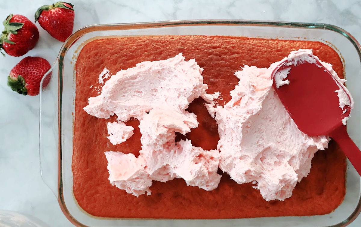 adding pink frosting made with buttercream frosting and strawberry jello onto the strawberry cake.