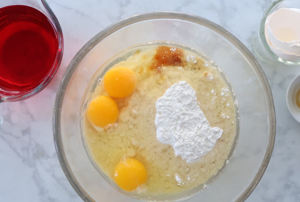 Cake mix, oil, eggs and vanilla for pink strawberry cake. Cup of red disolved jello to the side of the bowl.