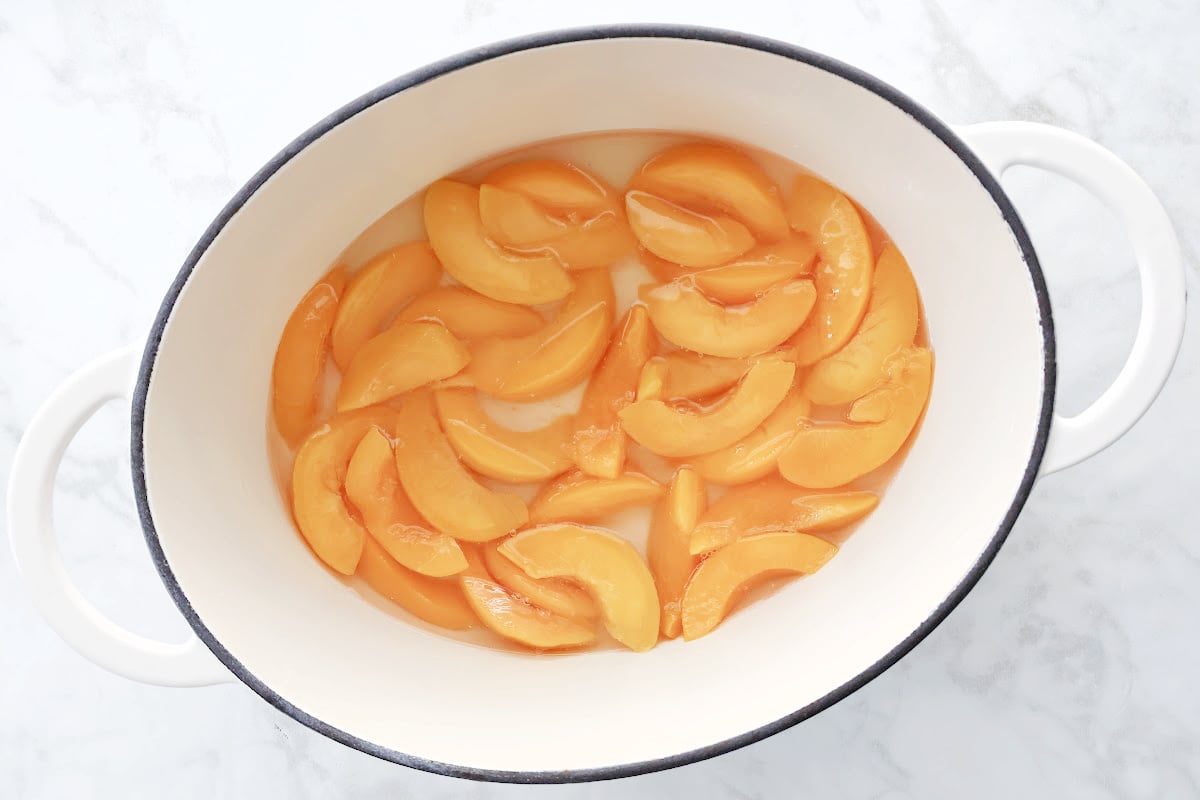 Peach slices being added to a greased dutch oven to make easy peach cobbler.