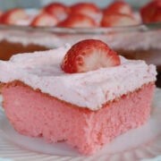 pink stawberry jello cake with pink buttercream icing on top. Garnished with a fresh strawberry.
