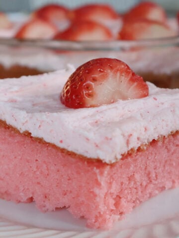 pink stawberry jello cake with pink buttercream icing on top. Garnished with a fresh strawberry.