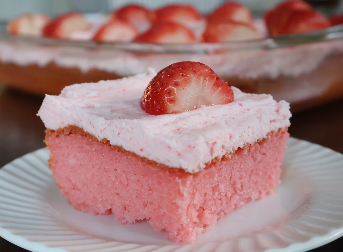 pink stawberry jello cake with pink buttercream icing on top.  Garnished with a fresh strawberry.