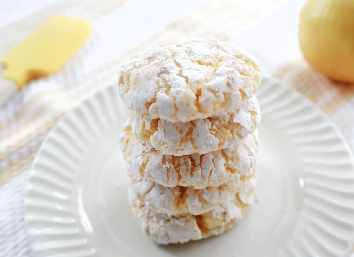 Soft lemon Cool Whip cookies coated in powdered sugar with crinkle tops on a white plate.