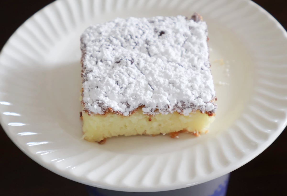 Slice of fluffy lemon bar dusted with powdered sugar served on a white plate.