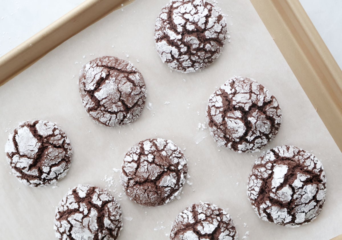 Chocolate crinkle cookies baking on parchment lined baking sheet showing the classic crinkle pattern forming.