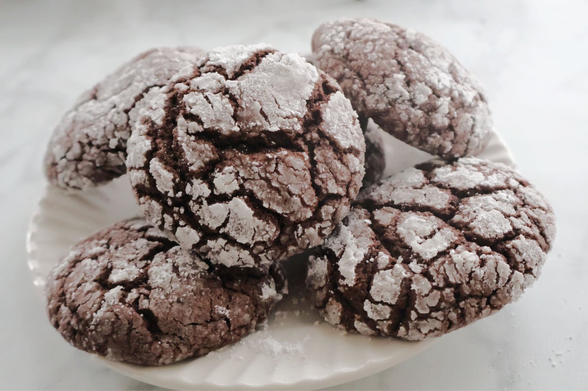 Close up of soft chocolate crinkle cookie showing powdered sugar cracks and fudgy interior.
