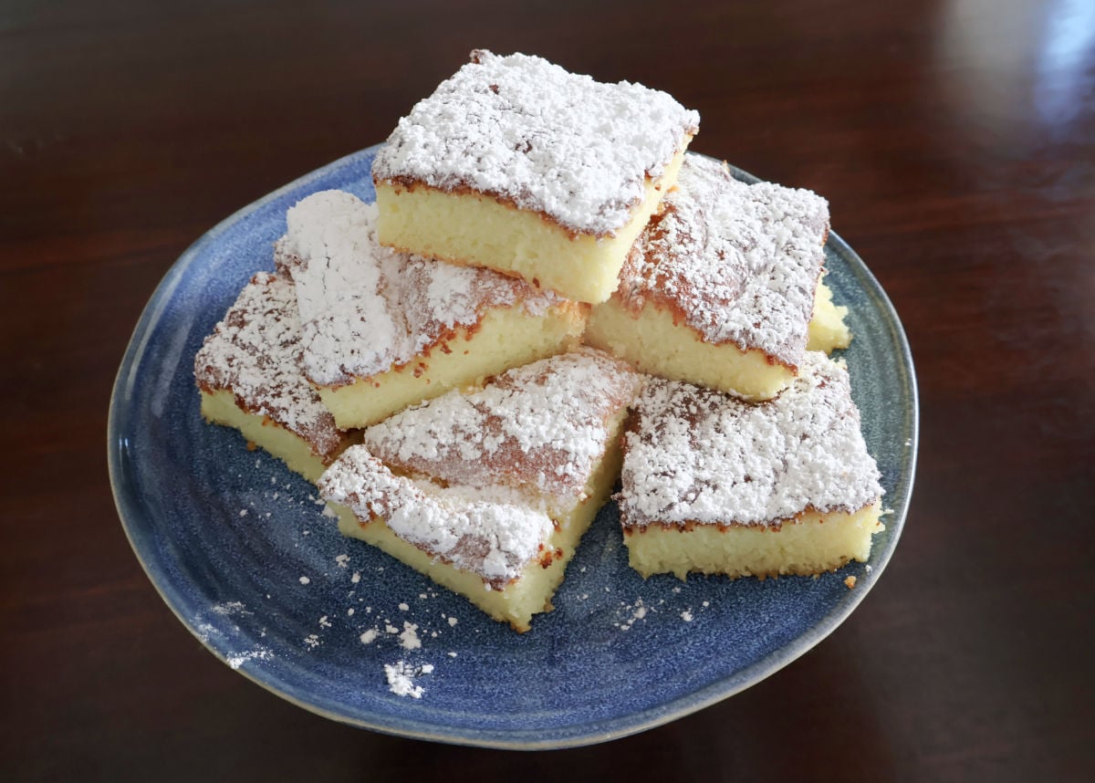 Lemon dessert bars dusted with powdered sugar and served on a plate.