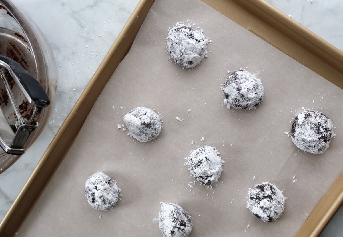 Cookie dough balls rolled in powdered sugar before baking chocolate crinkle cookies.