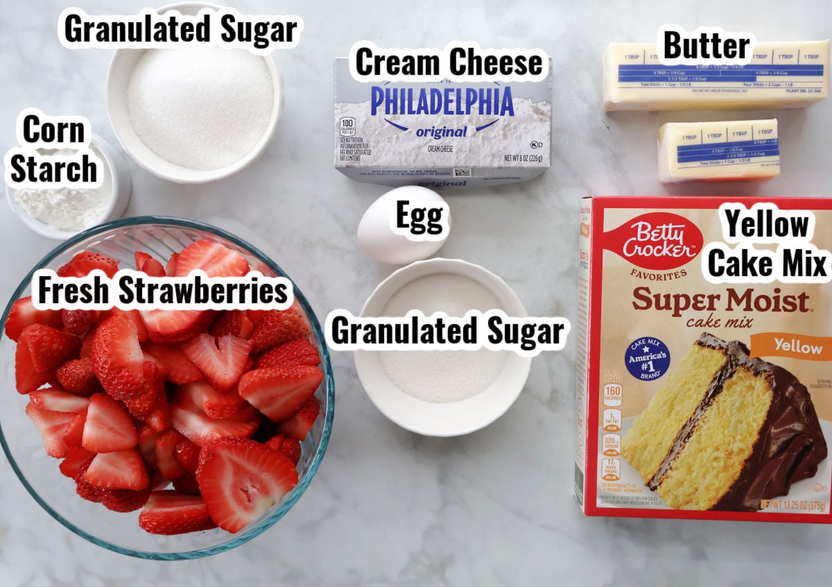 Ingredients for strawberry dump cake including fresh strawberries, cake mix, cream cheese, butter, and sugar