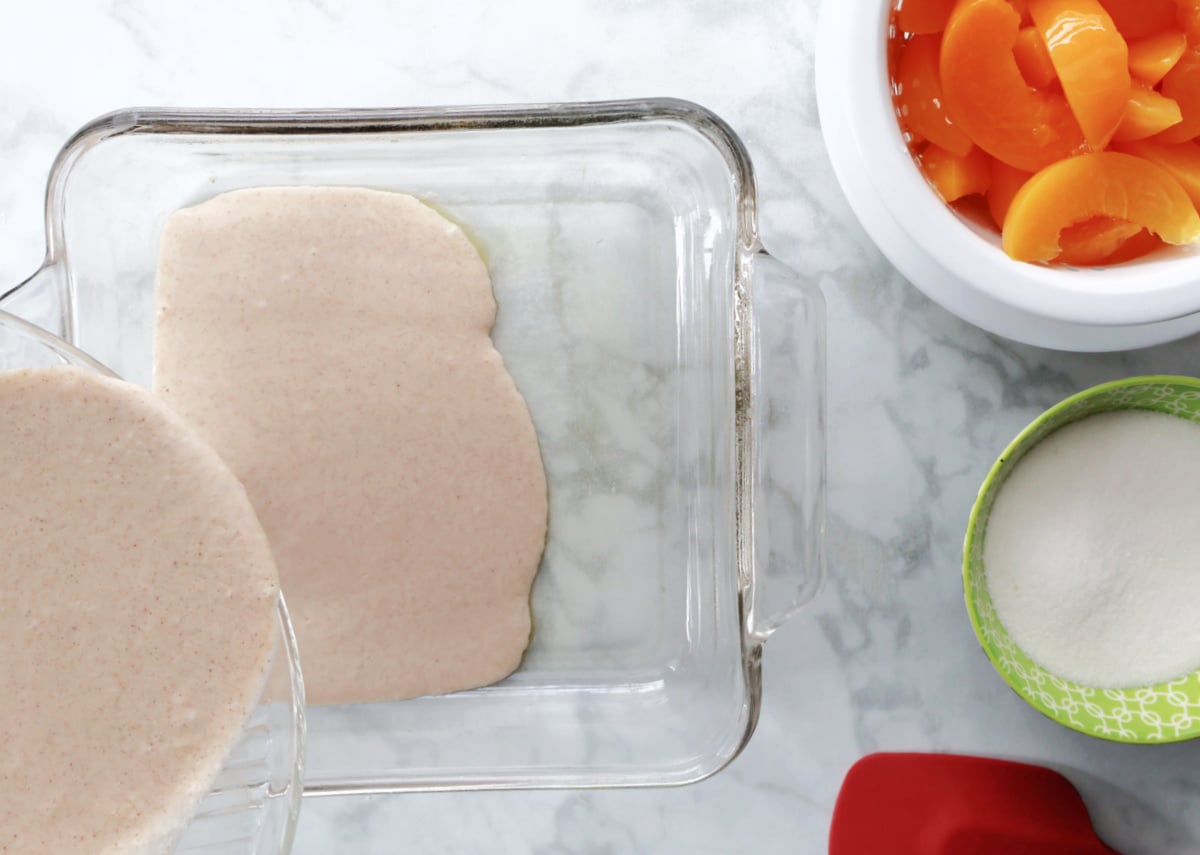 Peach cobbler batter made with Bisquick poured into a greased baking dish