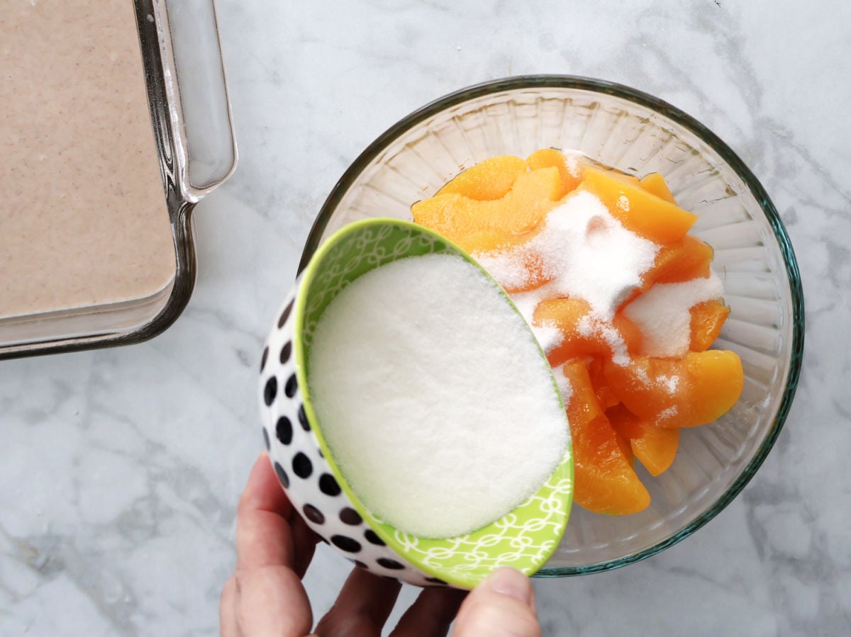 Sugar being added to sliced peaches for Biscuit Peach Cobbler recipe.