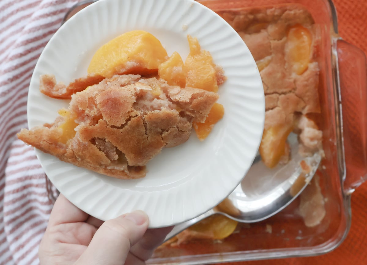 Spoon scooping warm Bisquick peach cobbler showing soft texture and peaches