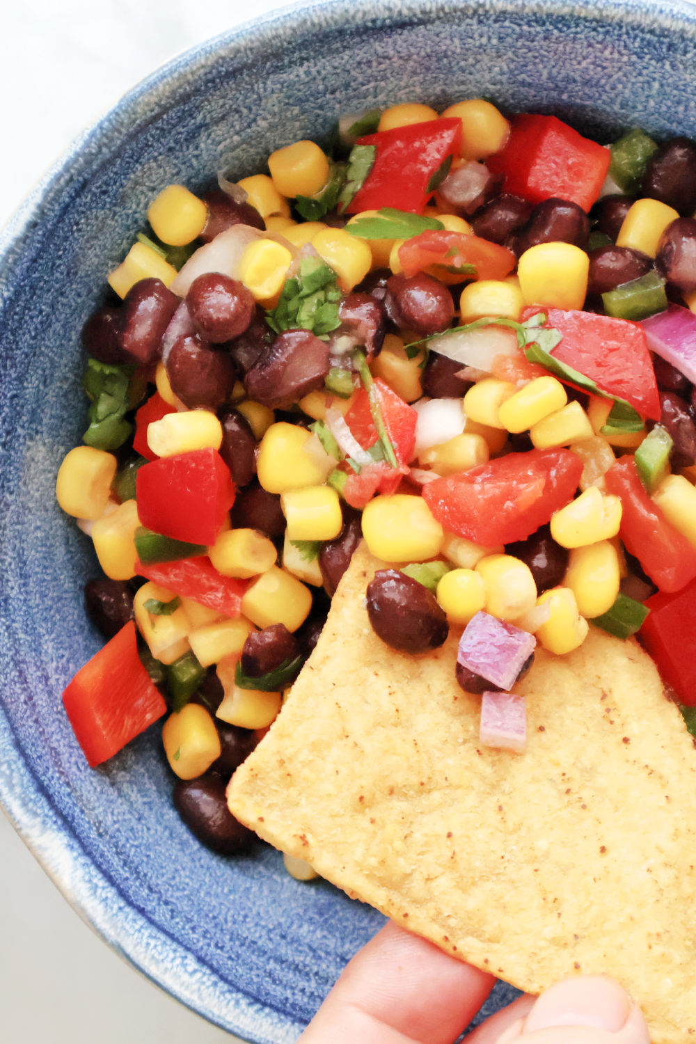 Easy black bean and corn salsa recipe in a serving bowl surrounded by tortilla chips.